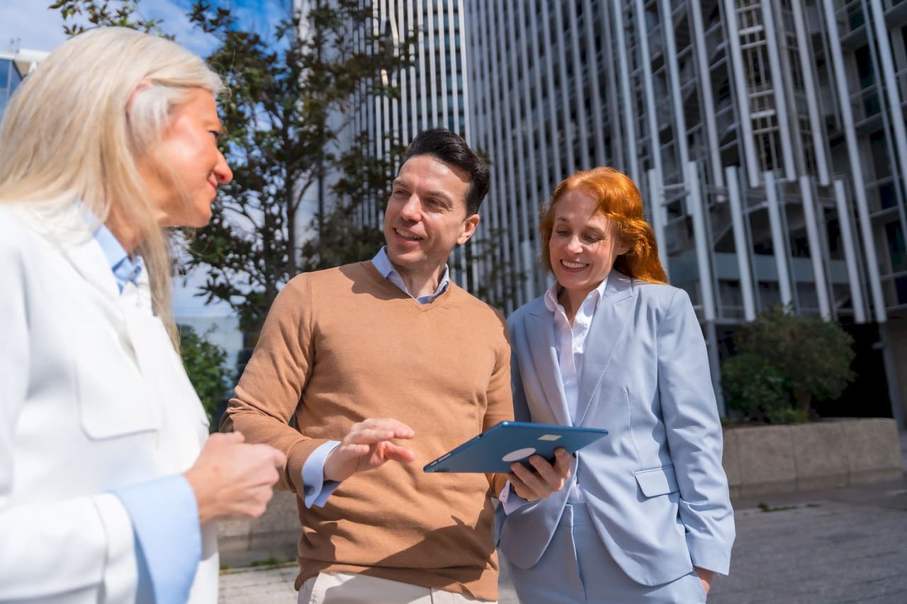 Three business people, two women and one man, having a discussion outdoors in front of a modern office building