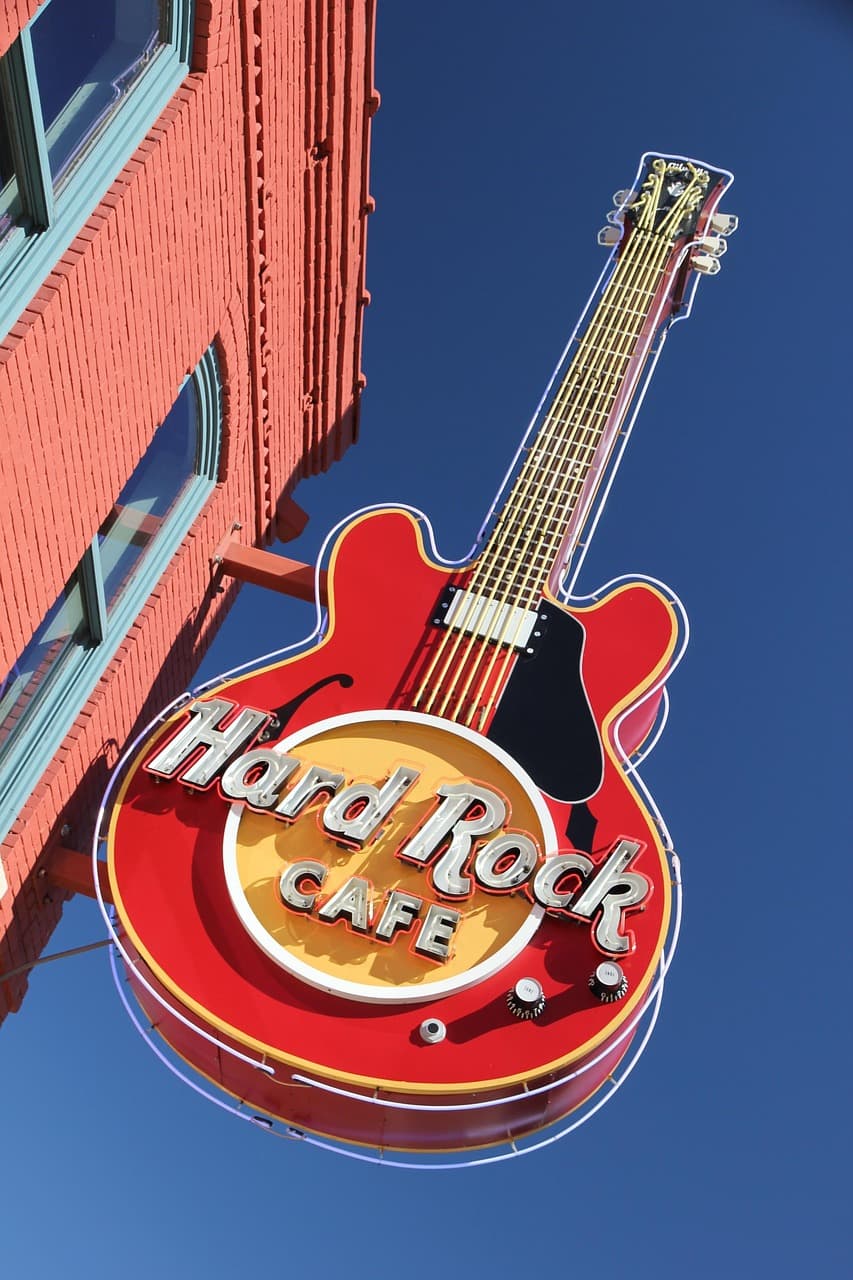 Red electric guitar shaped Hard Rock Cafe sign mounted on a brick building with clear blue sky background