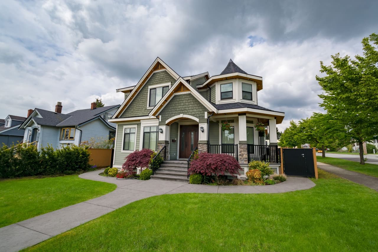 Large Victorian style house with a turret, front porch, and well-maintained lawn under a cloudy sky