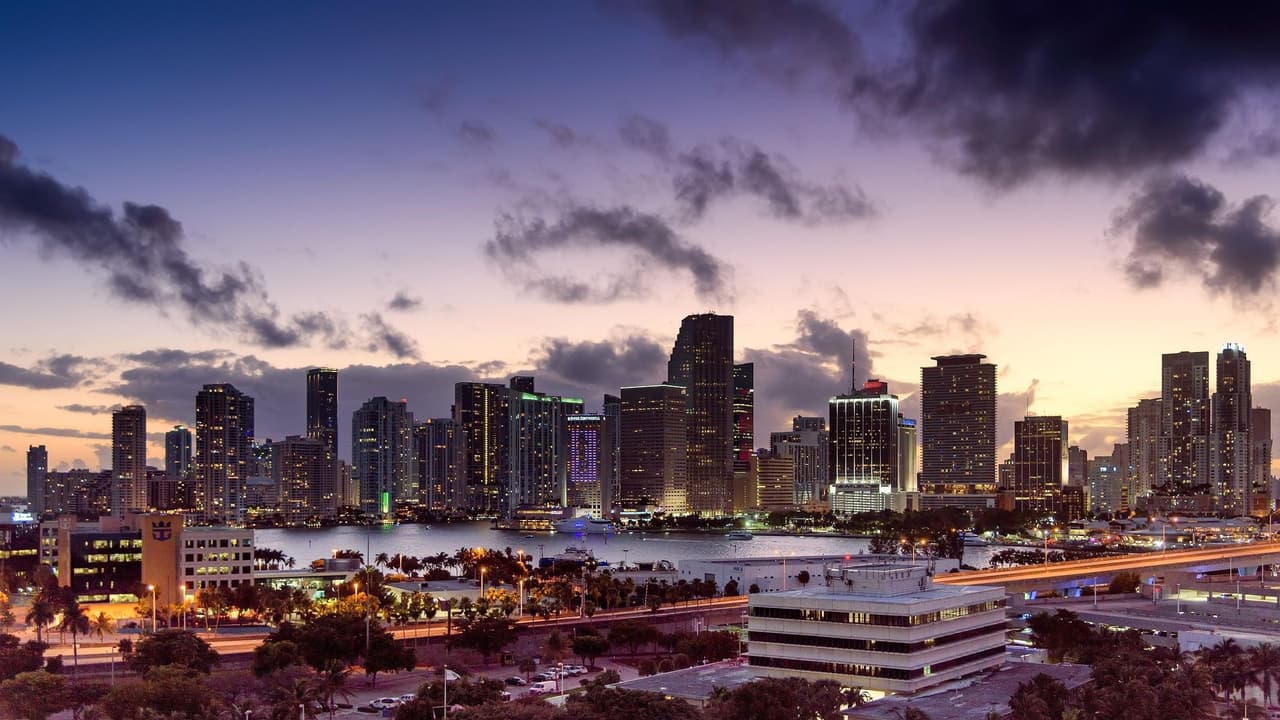 View of Miami city skyline at dusk with buildings illuminated and cloudy sky