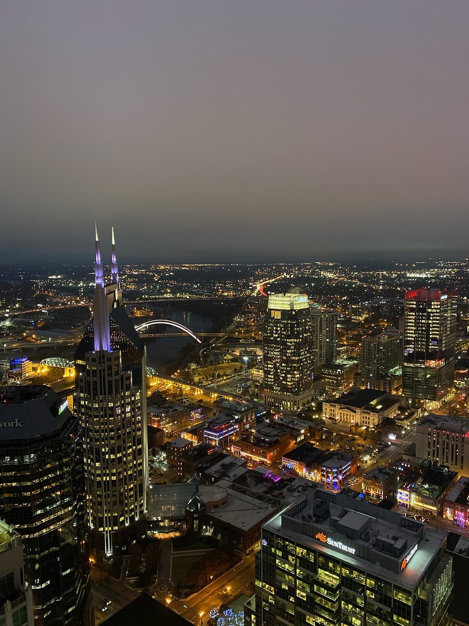 A nighttime aerial view of a city with illuminated skyscrapers and streets, including a prominent building with two lit spires, under a clear dark sky.