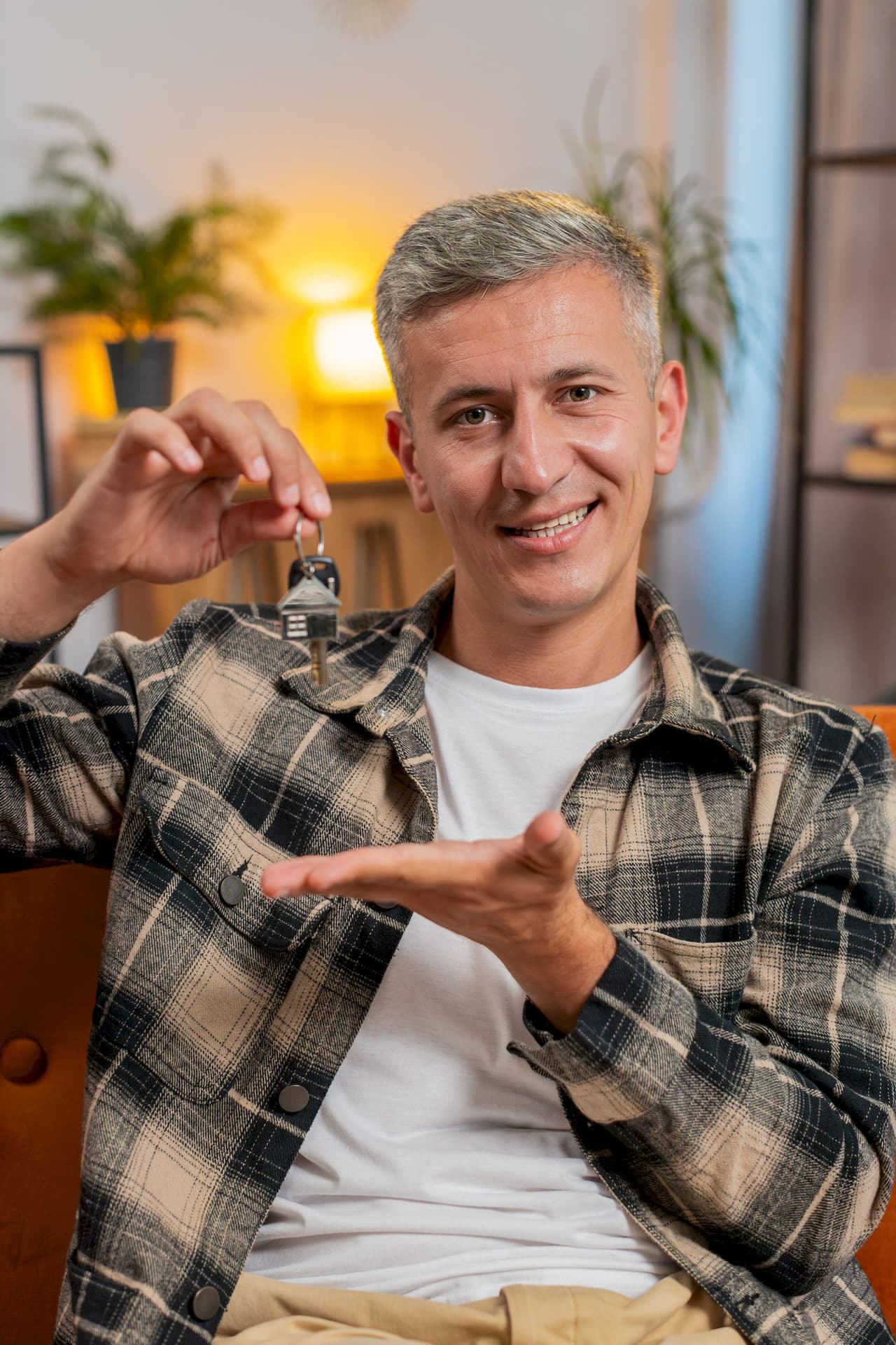 Smiling man holding house keys indoors with blurred background
