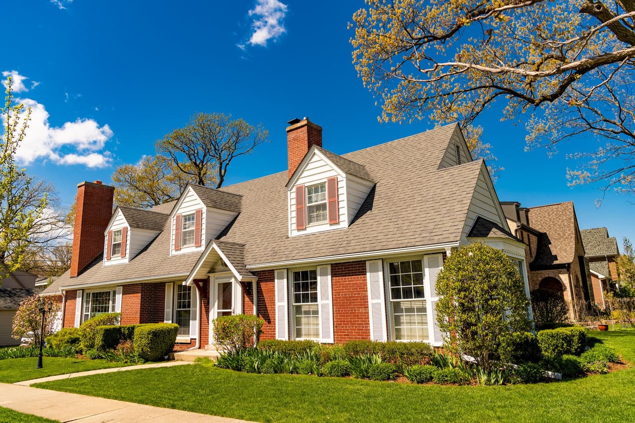 Suburban brick house with large windows and dormer windows on a sunny day with blue sky and some clouds