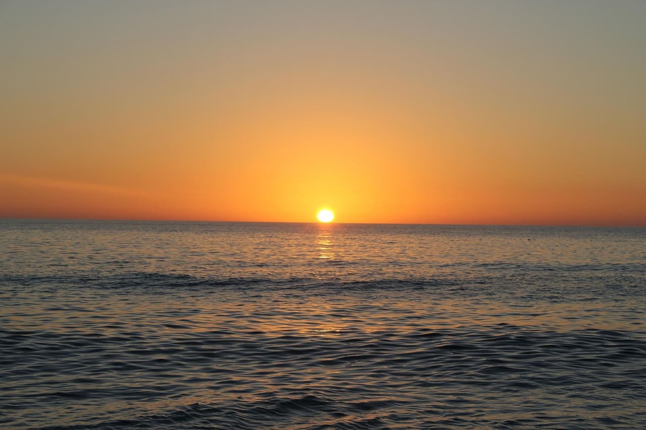 Sun setting over a calm ocean with gentle waves and an orange sky