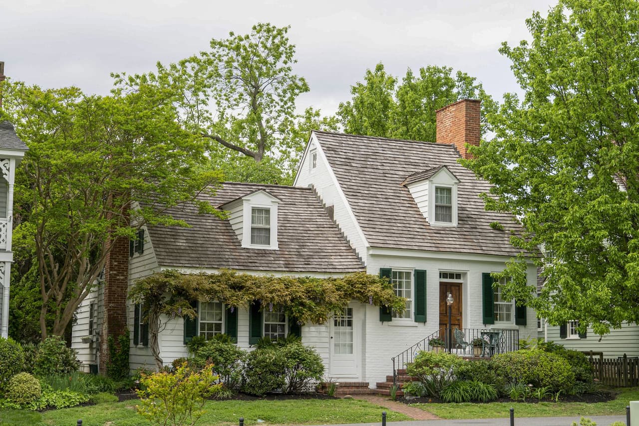 White cottage house surrounded by lush green trees and bushes