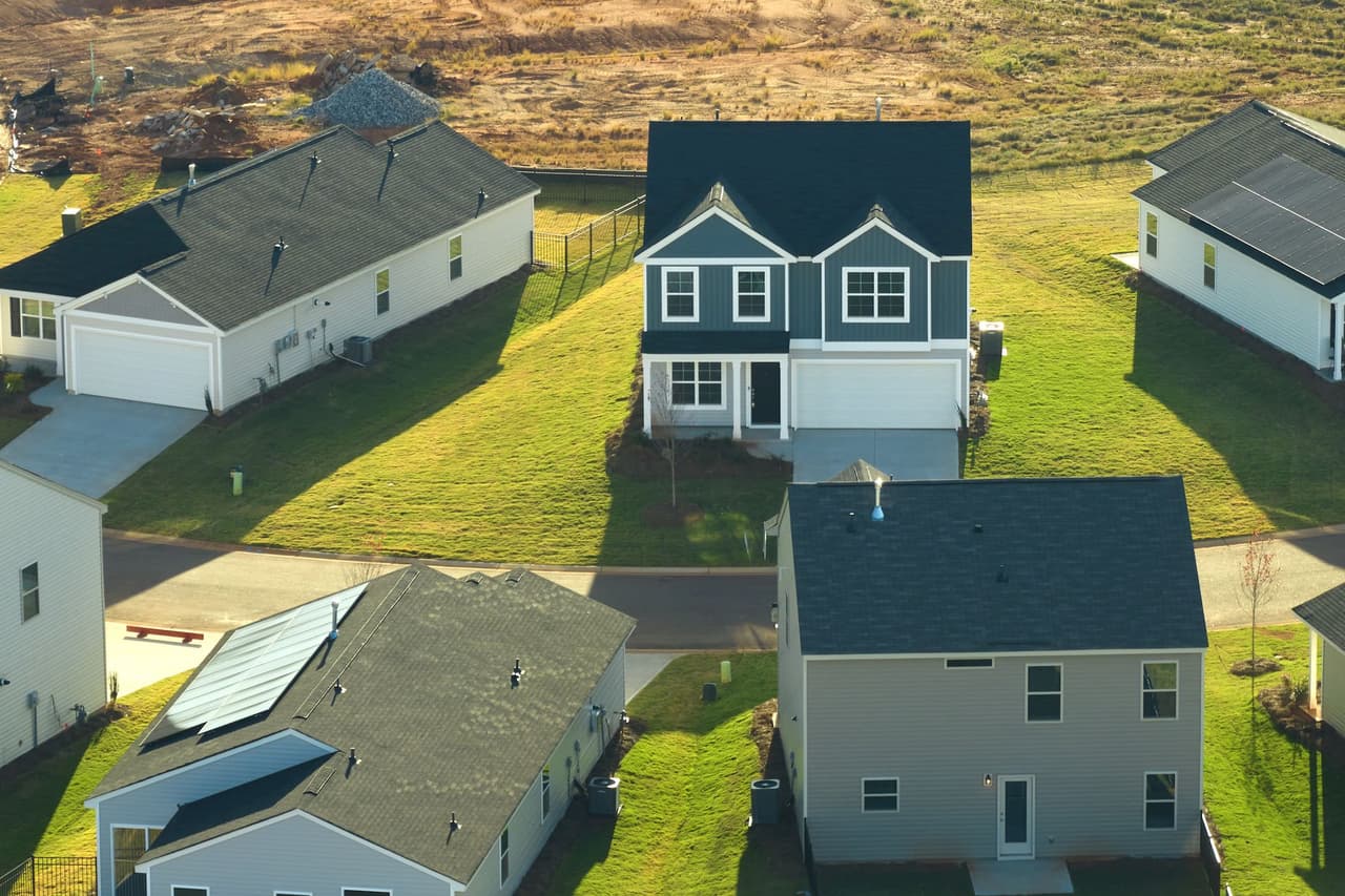 Aerial view of suburban houses with green lawns and a construction site in the background