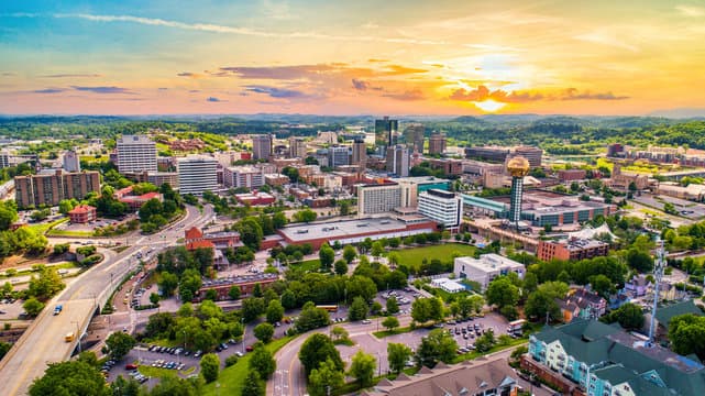 Aerial view of a city with buildings, roads, and green spaces during a colorful sunset.