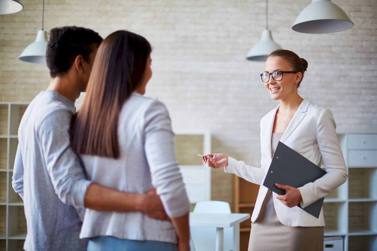Female real estate agent handing keys to a couple in a modern office setting
