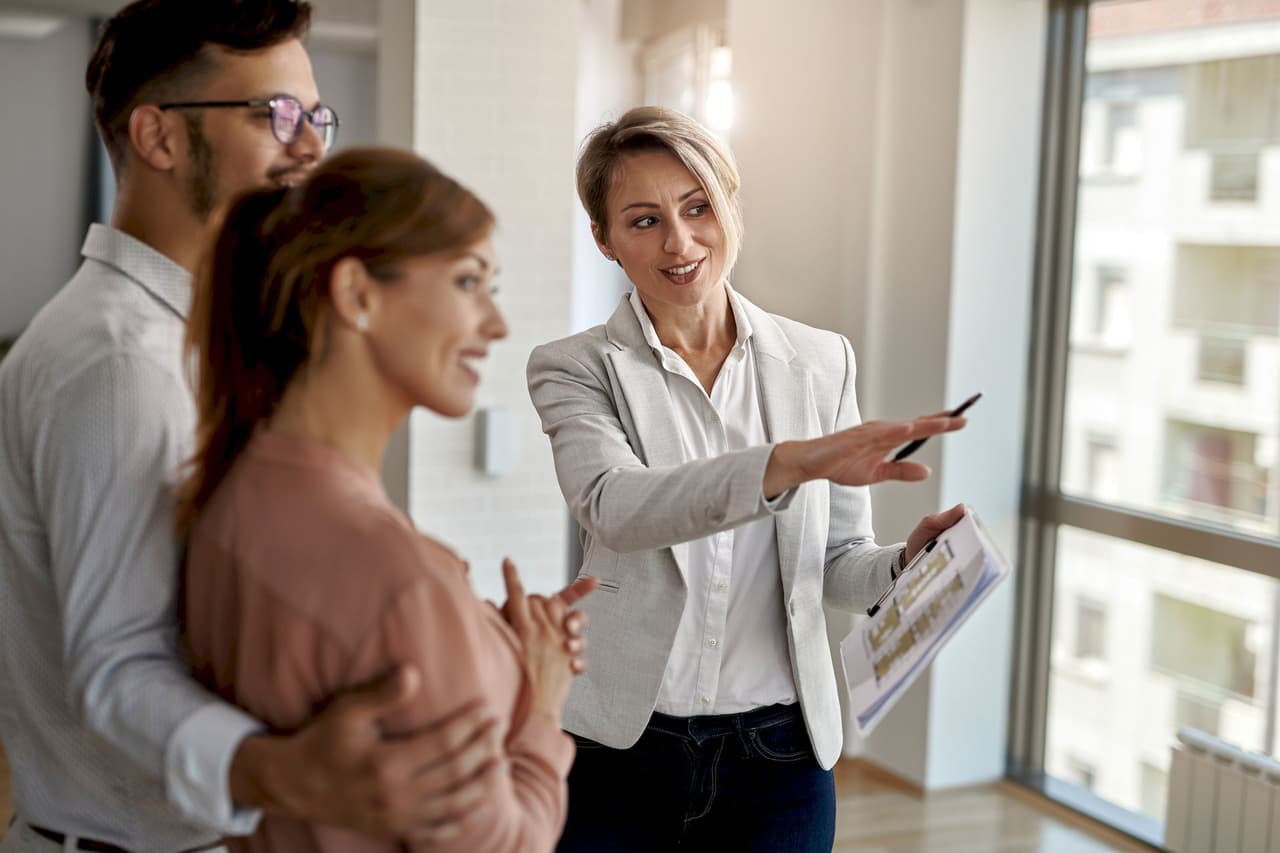 Female real estate agent showing property details to a couple inside a bright room with large windows