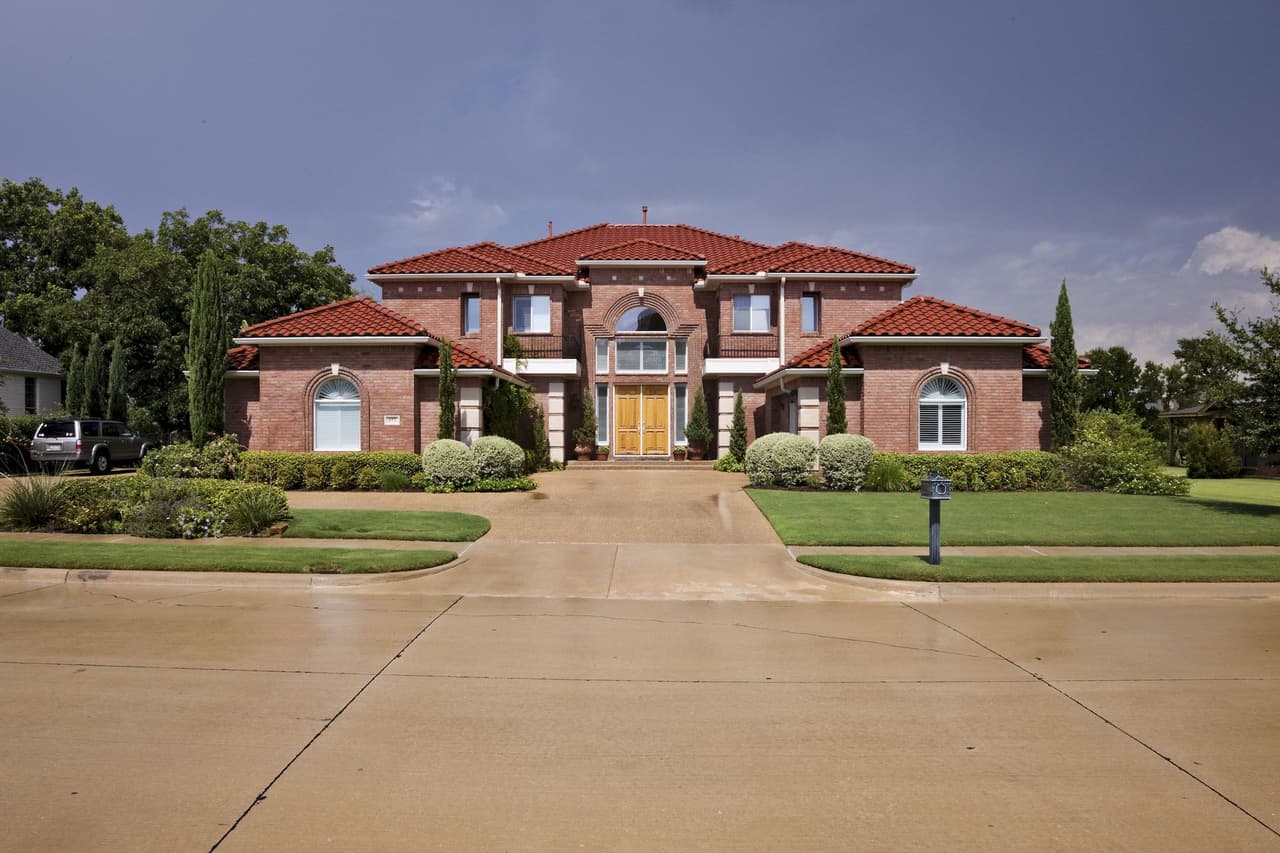 Front view of a large brick house with a red tiled roof under a clear blue sky