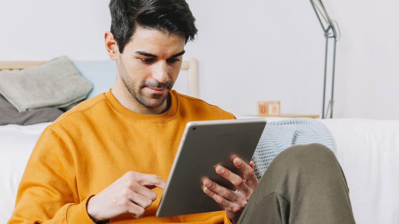 Young man wearing an orange sweater using a tablet indoors with a blurred background
