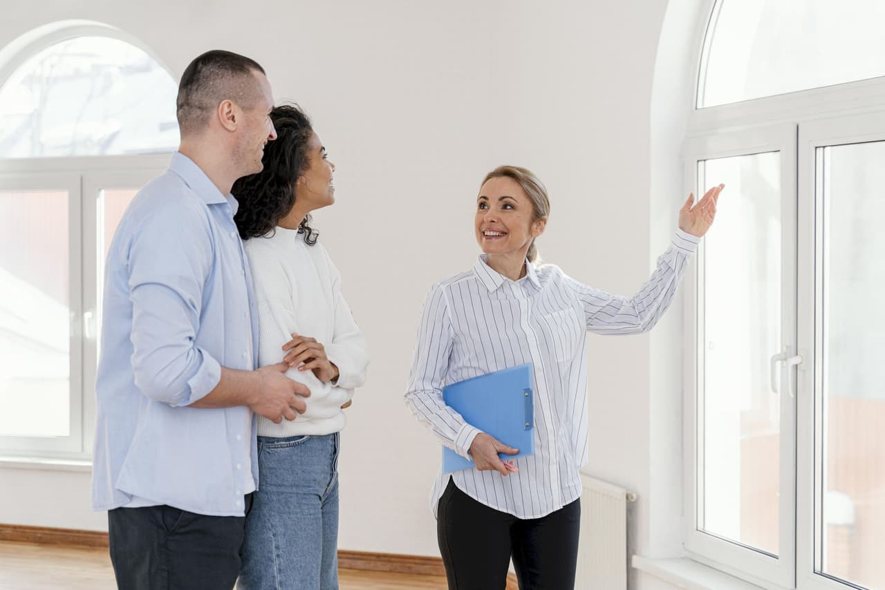 Female real estate agent showing a couple a bright room with large windows in a house