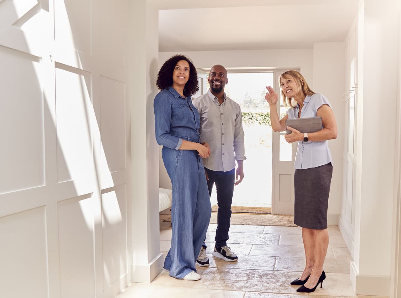 Real estate agent showing a smiling couple a home interior with natural light coming through the windows