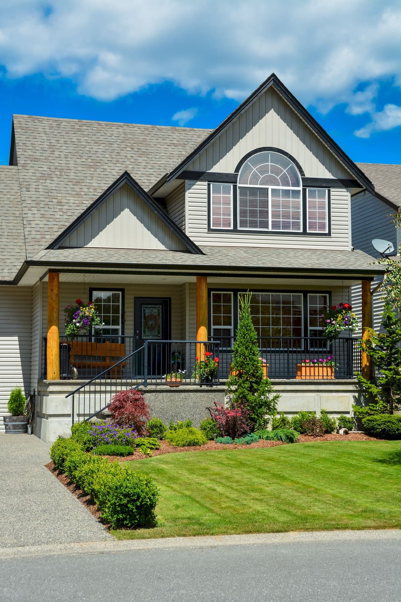 Front view of a suburban house with a well-maintained lawn, garden, and a porch under a partly cloudy blue sky