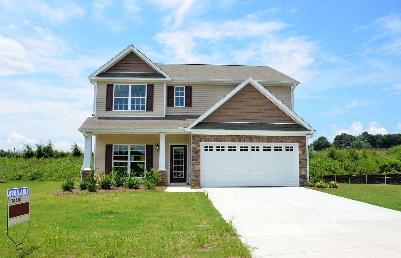 Front view of a suburban two-story family house with a garage and a well-maintained lawn under a blue sky with some clouds