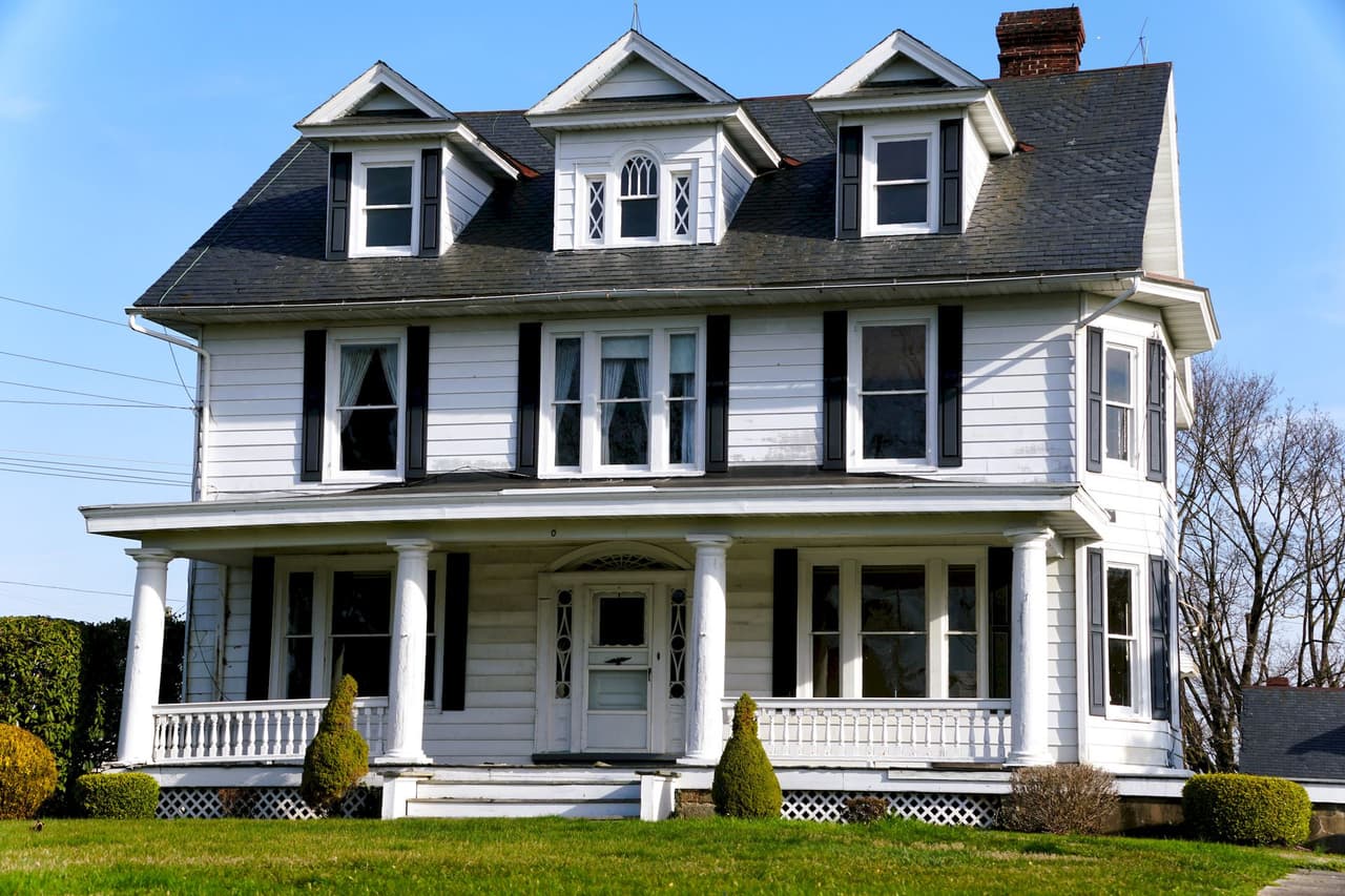 White Victorian style house with multiple windows, dormers, and a front porch, set against a clear sky and green lawn