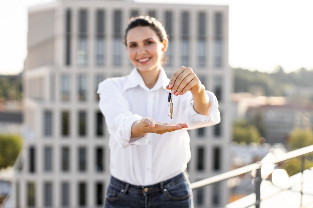 Portrait of a smiling woman holding a house key with a blurred cityscape background
