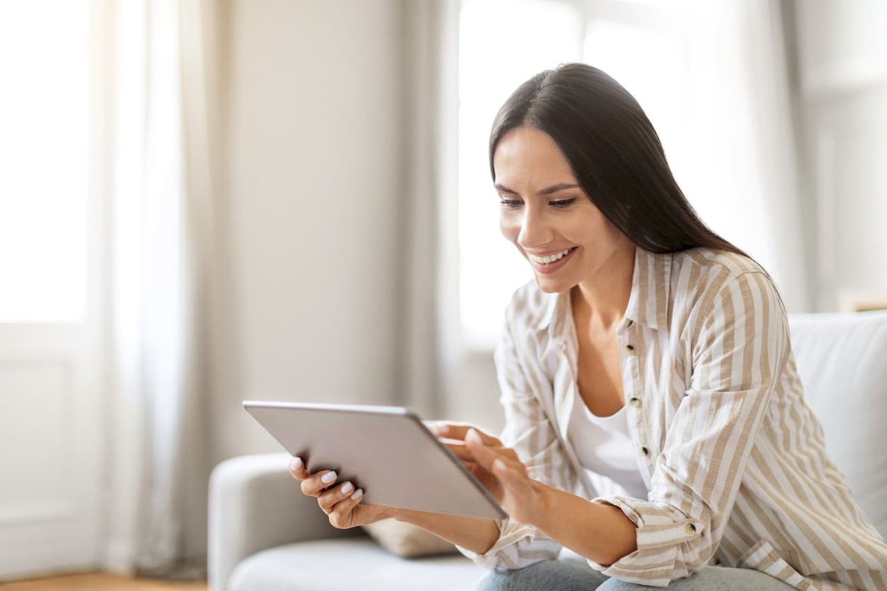 Smiling woman with long dark hair using a tablet indoors with a softly blurred background